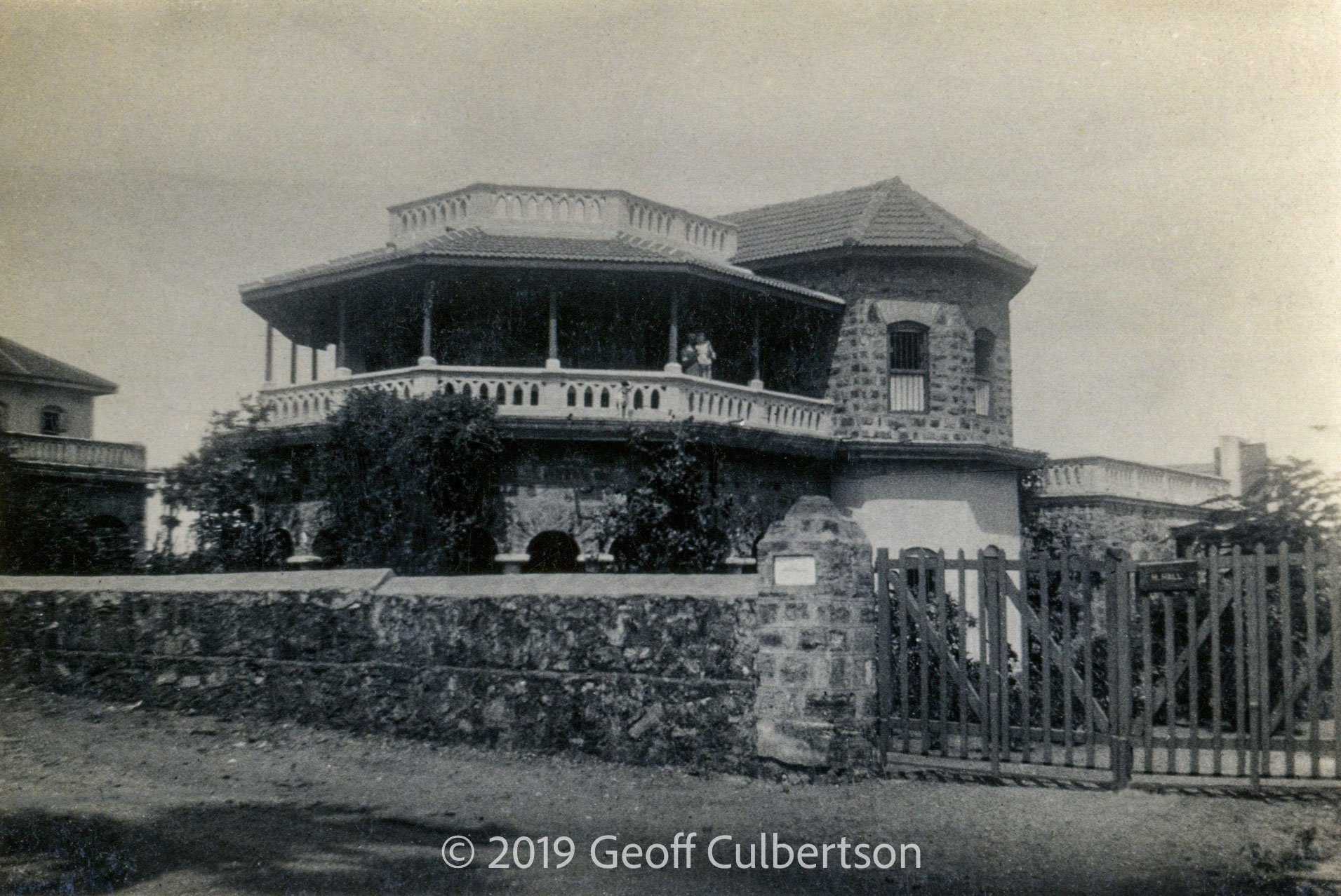Home of Hall family. Simonne & Kathleen on balcony. Nameplate 'H. Hall' on gate.